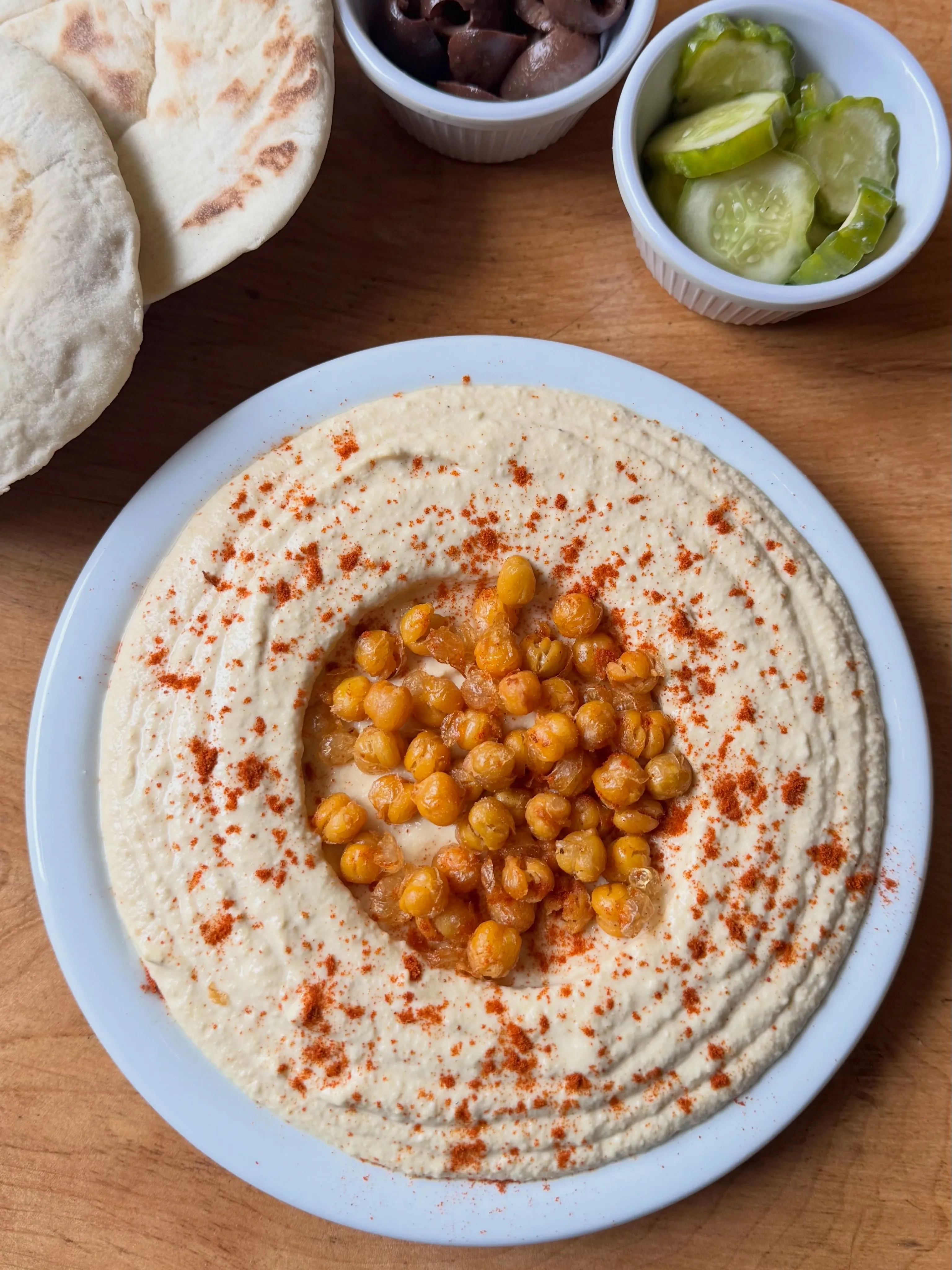 Plato de hummus cremoso con garbanzos fritos, pepinillos lactofermentados y aceite de oliva